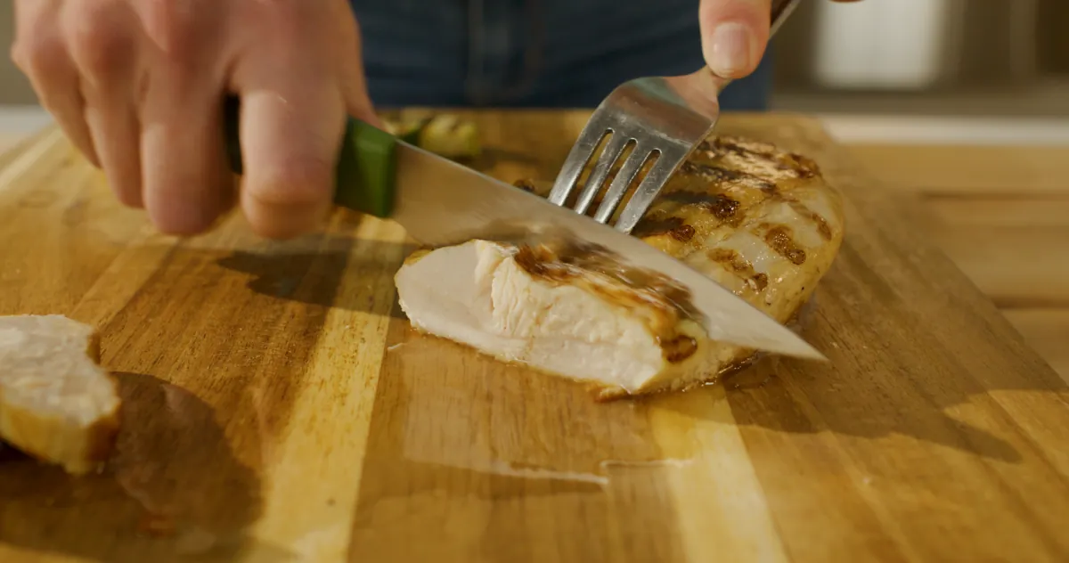 A grilled chicken breast with browned grill lines being sliced on a cutting board